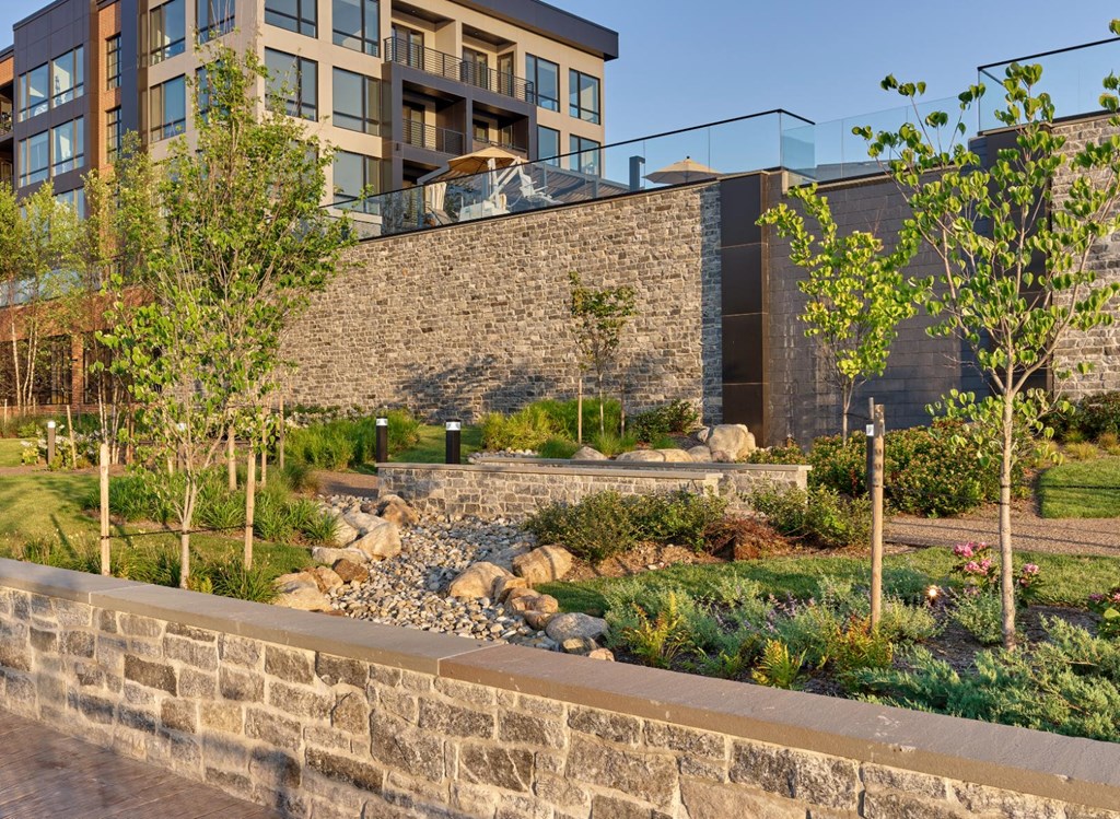 A modern building with a stone wall and a garden in front.
