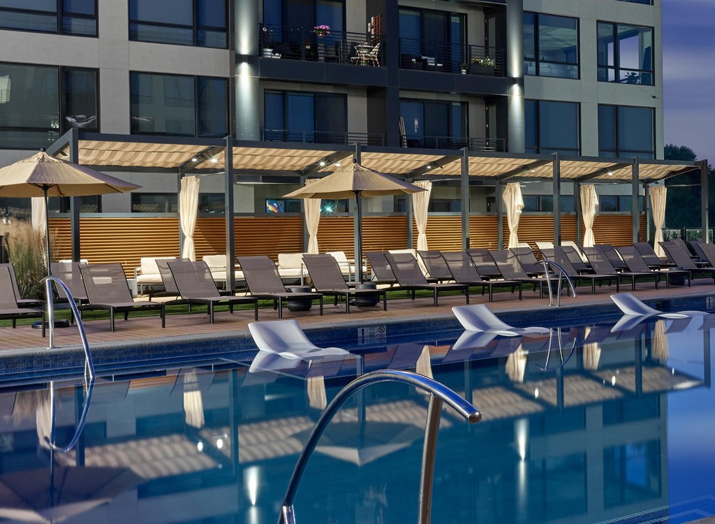A pool with sun loungers and umbrellas in front of a building.