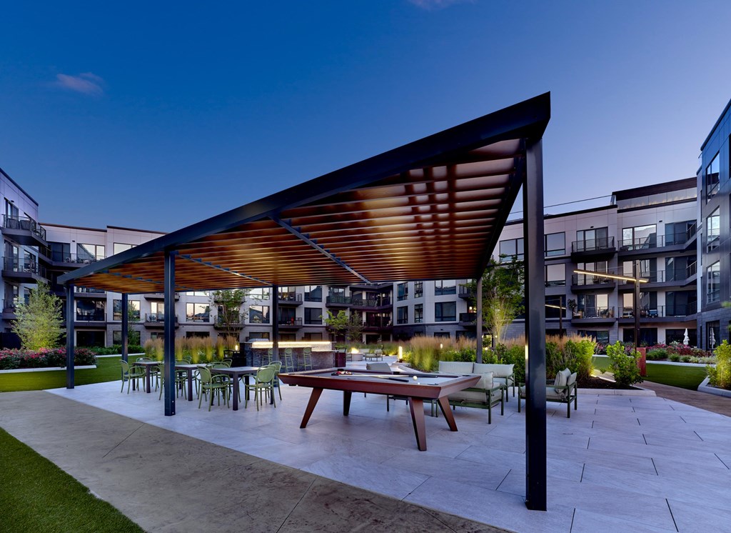 A patio with a table and chairs under a wooden roof.