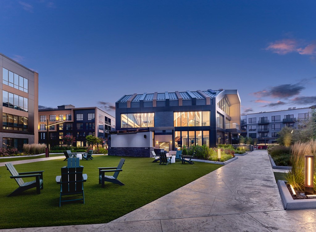 A modern building with a glass facade and a curved roof is surrounded by a grassy area with benches and a walkway.