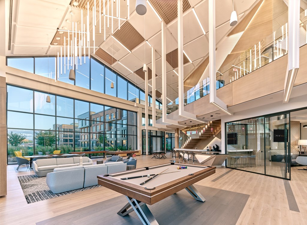 A billiard table is in the middle of a spacious room with a high ceiling and lots of windows.