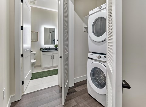 A white washing machine is in a laundry room with a mirror and a sink.