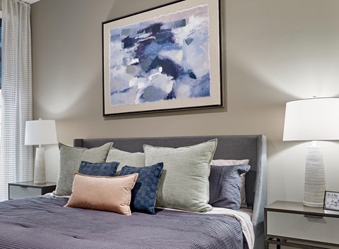 A bed with a purple comforter and a painting above it.
