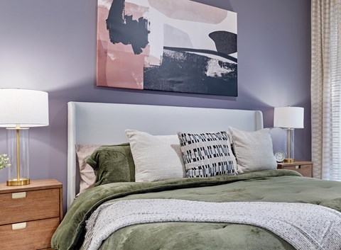 A bed with a green blanket and pillows in front of a painting.