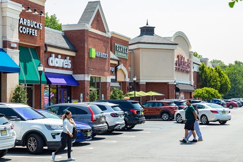 A woman is walking in a parking lot in front of a shopping center.