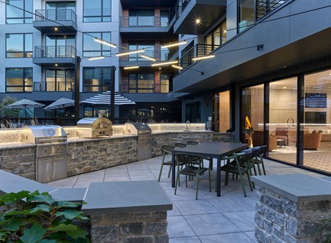 A patio area with a table and chairs is surrounded by a stone wall and a building with balconies.