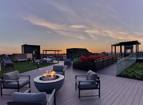 a patio with chairs and a fire pit on a roof at sunset