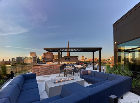 a patio with blue couches and a fire pit on a rooftop overlooking the city