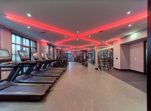 a gym with cardio machines and a row of red lights on the ceiling