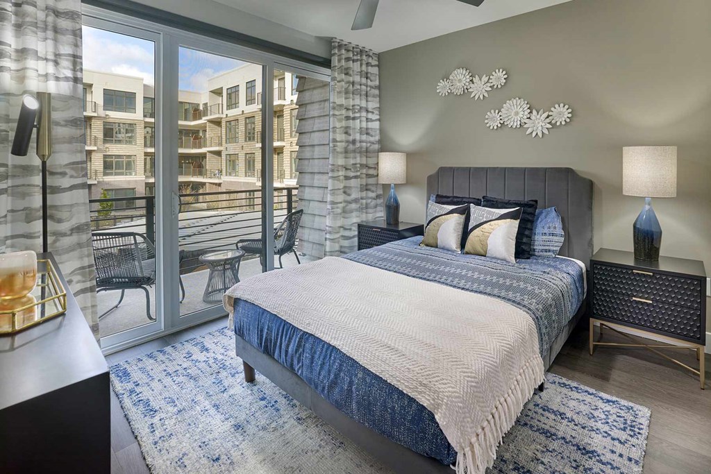 A bedroom with a large bed and a view of a balcony with chairs.