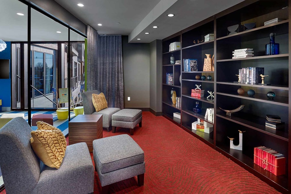 A room with a grey chair and a grey ottoman with a yellow pillow.
