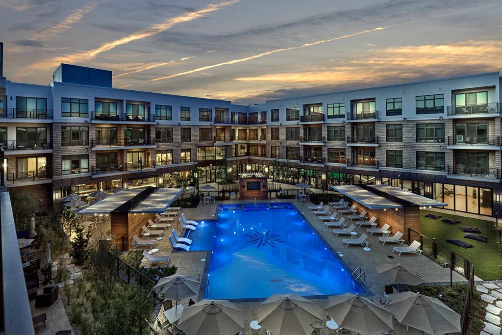 A large swimming pool surrounded by lounge chairs and umbrellas is the focal point of this luxurious apartment complex.