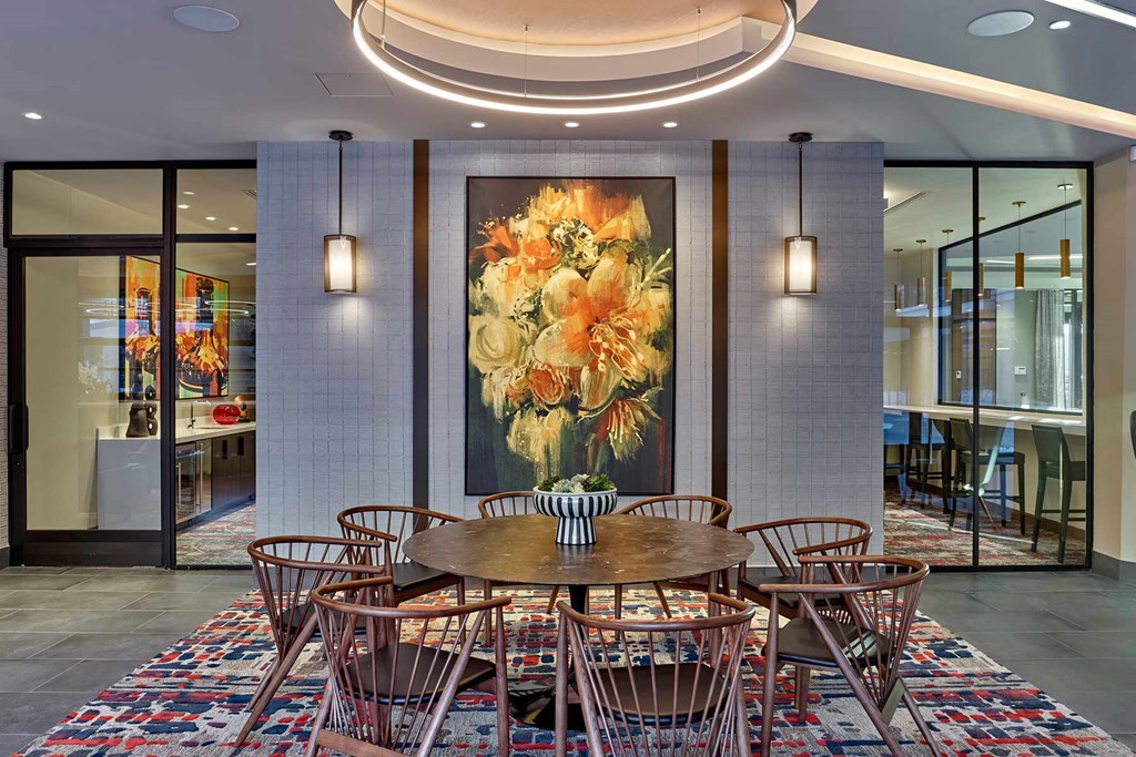 A large floral painting hangs above a round wooden table with chairs around it.