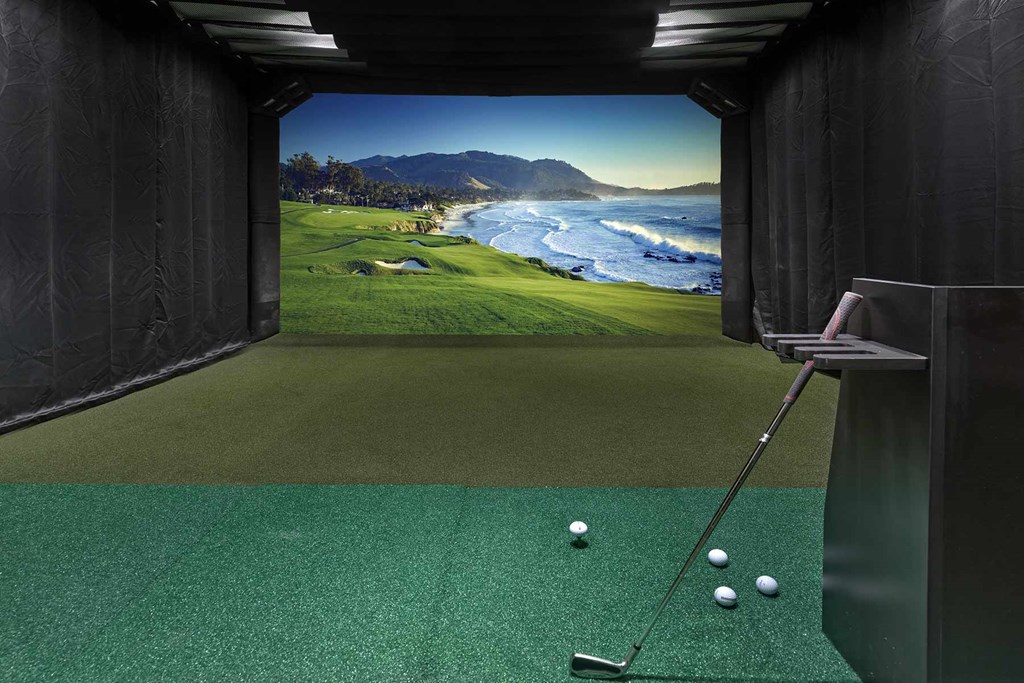 A golf simulator room with a green carpet and a screen showing a golf course.