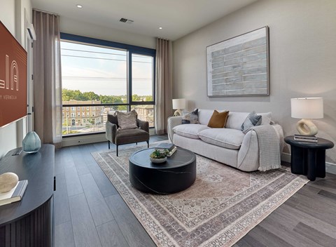 A living room with a white sofa and a large window overlooking a cityscape.
