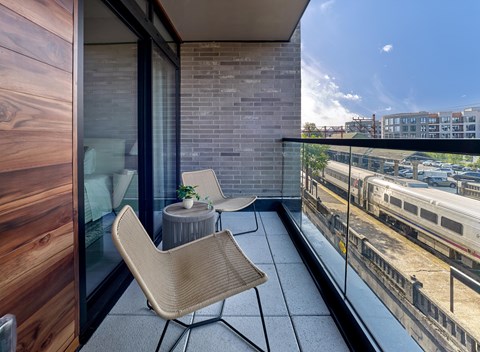 A balcony with a chair and a table overlooking a train track.