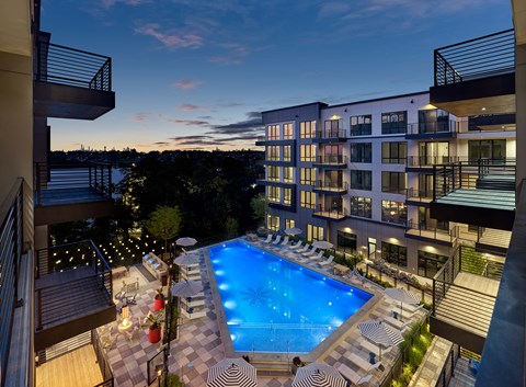 A swimming pool surrounded by lounge chairs and umbrellas is seen from a balcony.