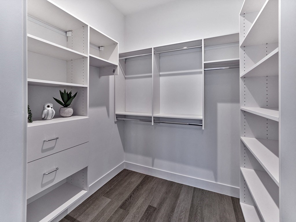 a white walk in closet with white shelves and drawers