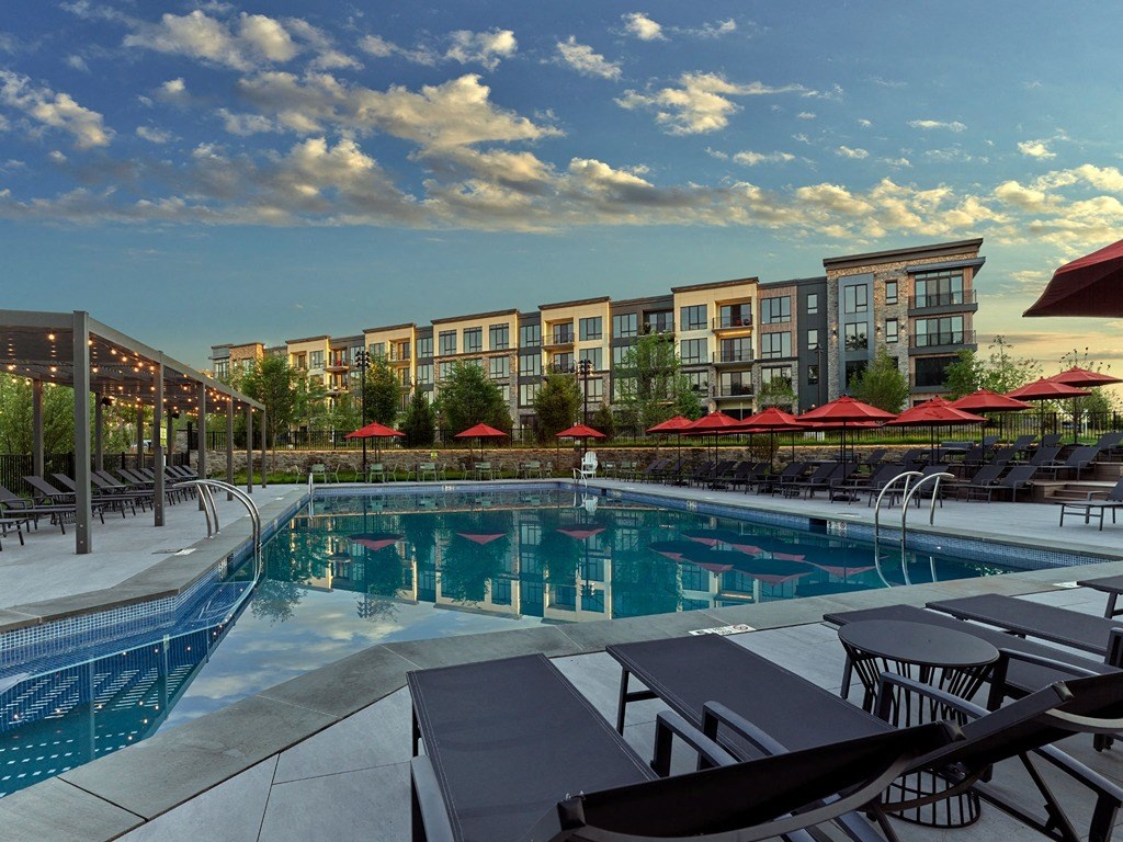 a swimming pool with tables and umbrellas in front of an apartment building