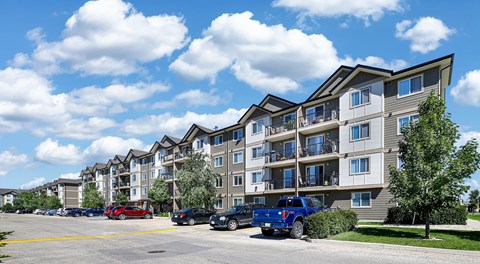 A row of apartment buildings with cars parked in front.