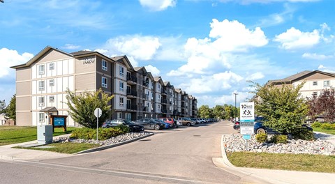 A row of apartment buildings with cars parked in front.