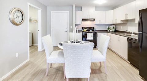 A bright open kitchen, with light cabinets and black appliances. A round table sits in the middle with four chairs