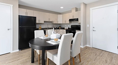 A kitchen with light cabinets, black appliances and an oval table