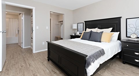 A bedroom with a queen bed, nightstand, and an opening to a walk in closet