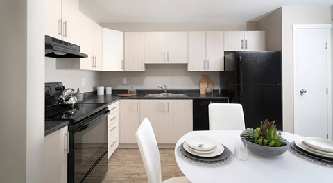 A modern kitchen with black countertops and light cabinets, black appliances. a kitchen table set of four sits in the center