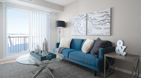 a living room with couch, coffee table, end table and lamp. Large glass sliding door leading to balcony
