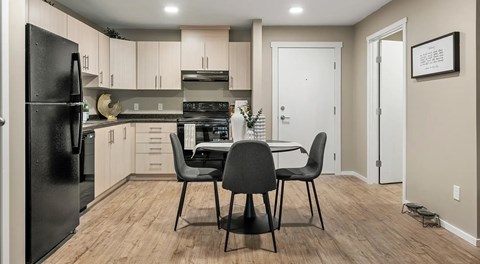 A bright open kitchen with light cabinets and black appliances with a round table in the centre