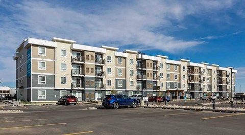 A four storey apartment building with large parking lot in front