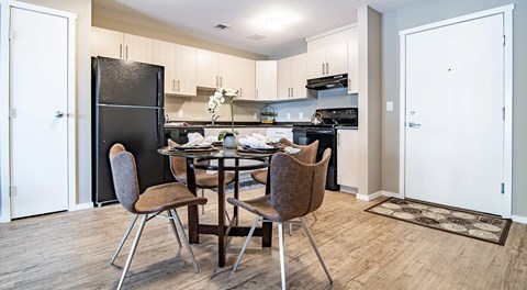 A kitchen with a small pantry, light cabinets and black appliances. A kitchen table sits in the centre of the kitchen