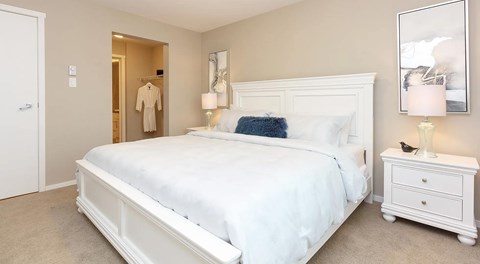 A white bedroom with a large bed, nightstand, and a painting on the wall.