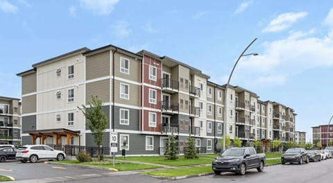 Apartment building with cars parked in front. and a parking lot to the side of the building