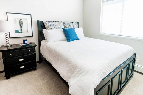 A bedroom with a white bed and a black nightstand.