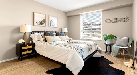 A bedroom with a queen sized bed, two nightstands and a chair with a large window.