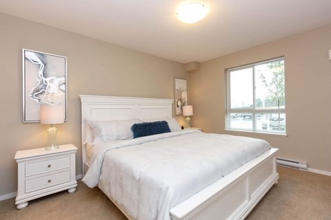 A bedroom with a white bed and a white nightstand with a lamp on it.