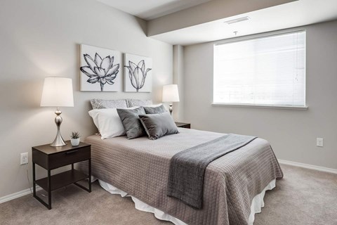 A bedroom with a bed, two lamps, and two paintings on the wall.