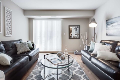 A living room with two black leather couches and a glass coffee table.