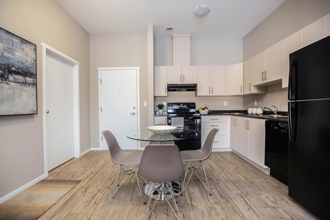 A kitchen with a black fridge, white cabinets, and a table with four chairs.