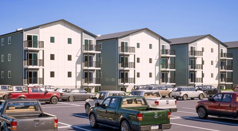 A row of four apartment buildings with blaconies at the ends with a parking lot in front