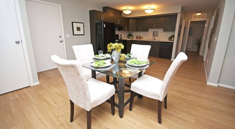 A warm lit kitchen with dark cabinets, light counter tops and black appliances, a large open space with a kitchen table set for four