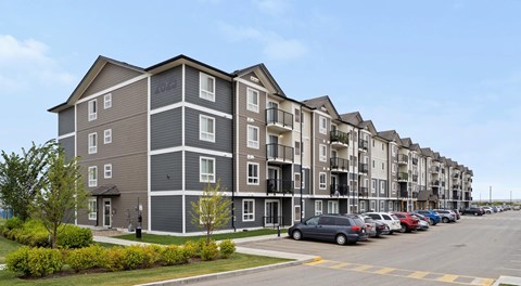 Apartment building with grey and white exterior and a parking lot in front.