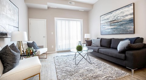 A bright open living room with couch, two chairs a coffee table and end tables. A big glass sliding door on one wall
