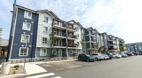 A row of modern apartment buildings with parking in front.