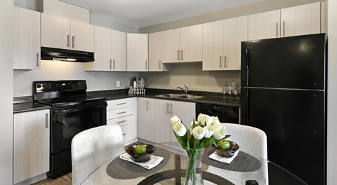 Modern kitchen with light cabinets and black appliances with a kitchen table in the centre
