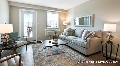 A bright open living room with a couch, chairs and coffee table. A single patio door with window next to it and wall mounted AC unit below