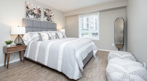 A bedroom with queen sized bed, night stands and dog bed. A window with blinds on the outer wall