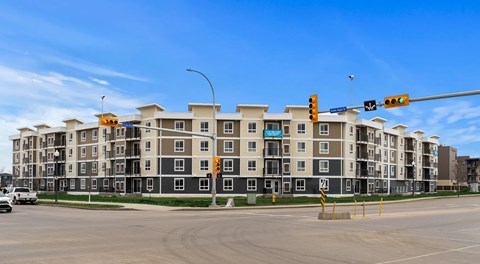 A large apartment complex sits at the corner of an intersection with a large curved building.